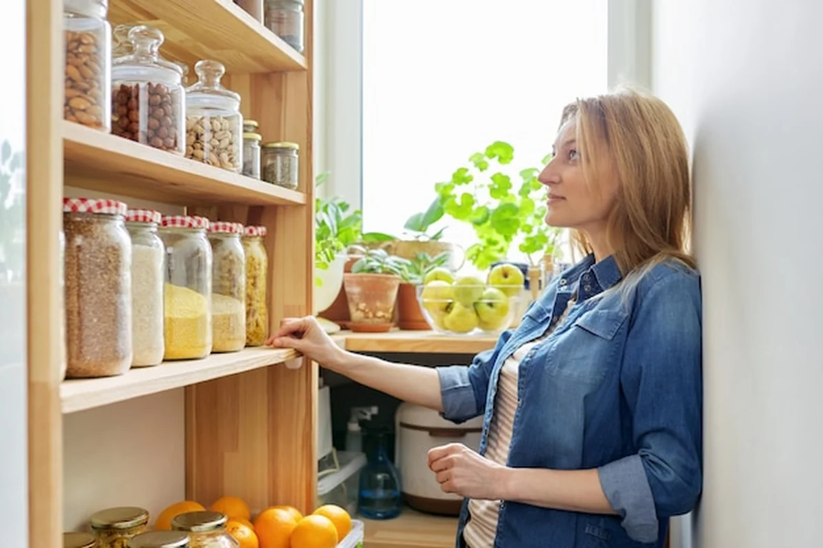 Kobieta w kuchni przy drewnianym stojaku z jedzeniem w słoikach i pojemnikach