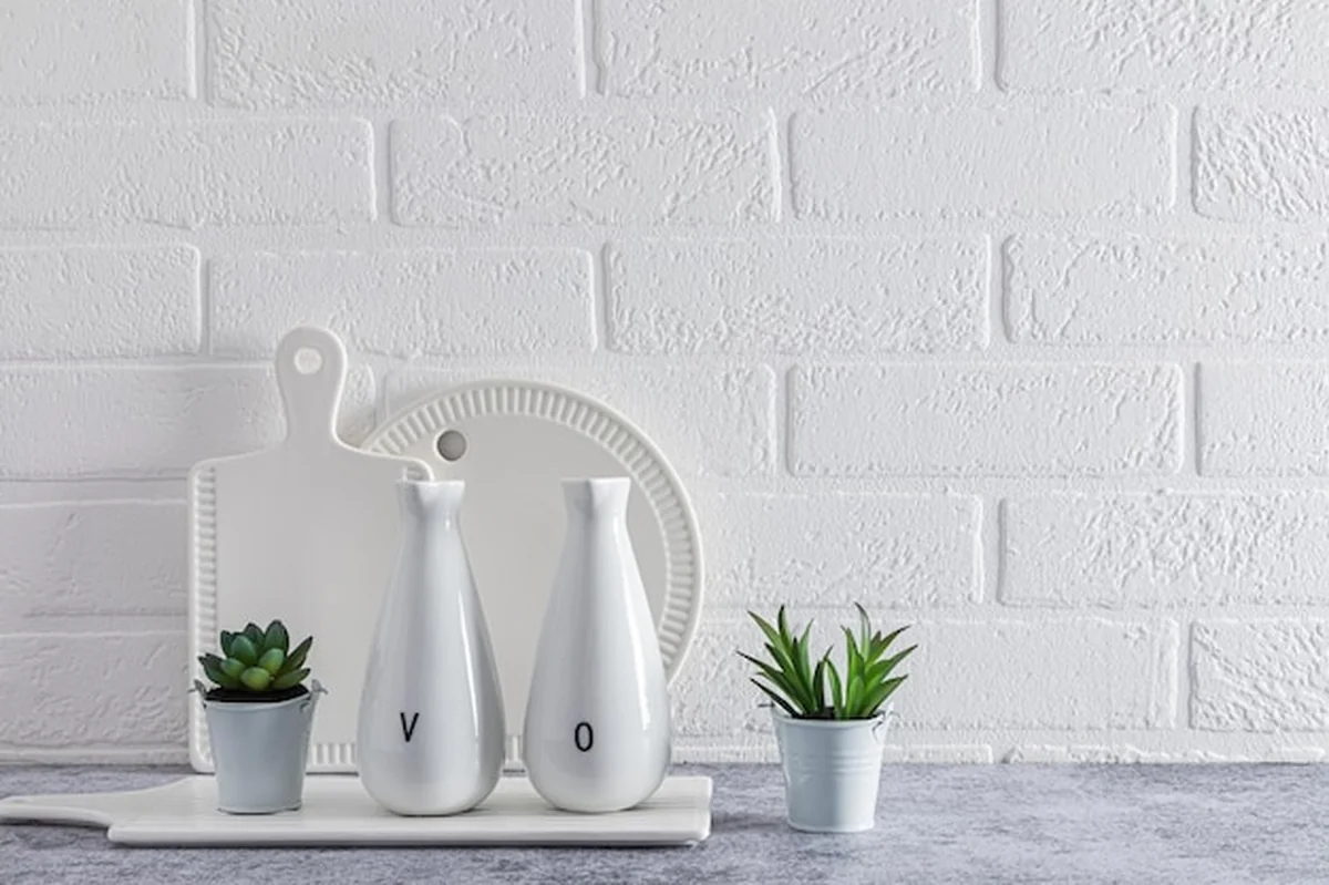 Białe przybory kuchenne na marmurowym blacie przed białą ceglaną ścianą z roślinami