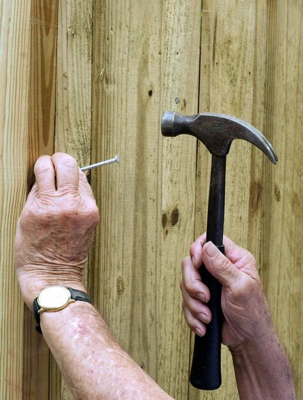 Osoba uderzająca gwoździem w drewniany płot