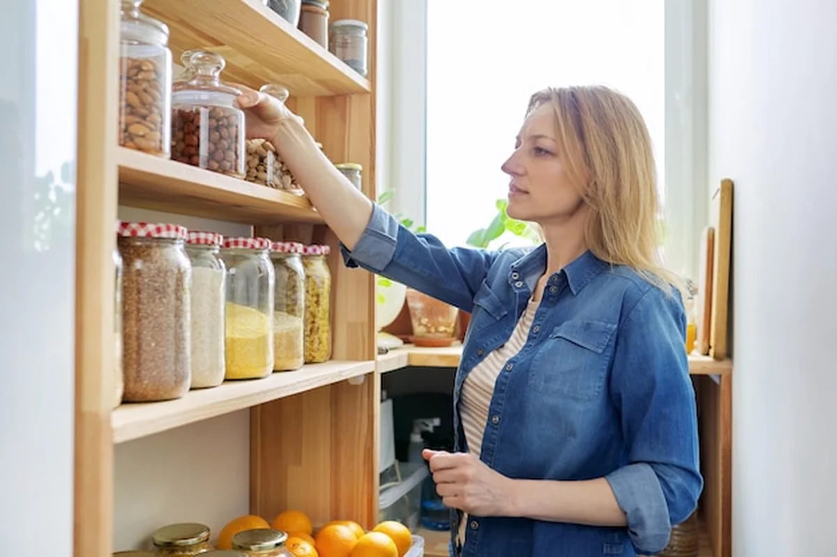 Kobieta w domowej kuchni przy drewnianym stojaku z jedzeniem w słoikach i pojemnikach